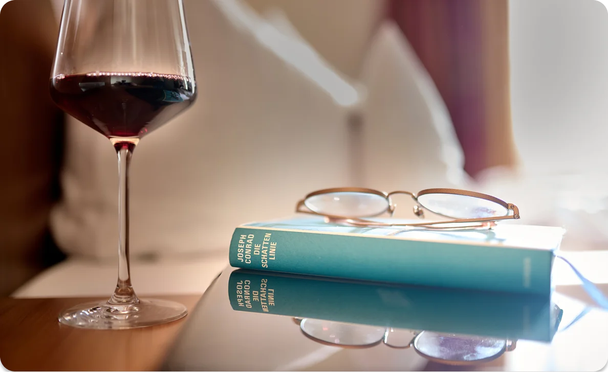 Weinglas, Buch und Brille auf Tisch